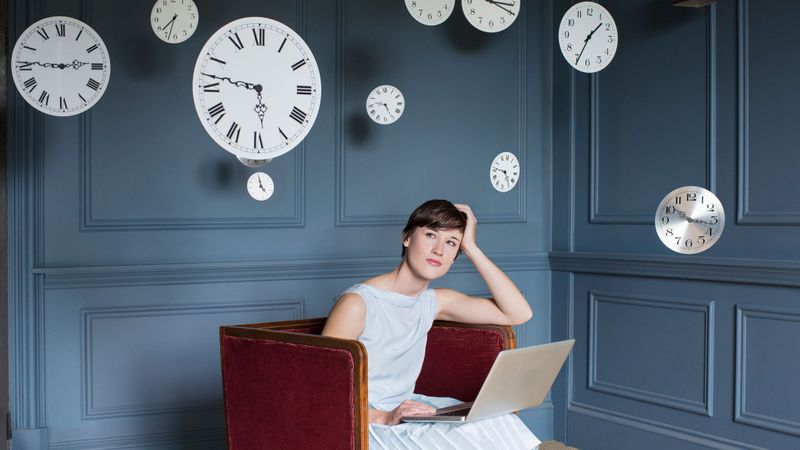 Lady sitting down with a laptop surrounded by clocks